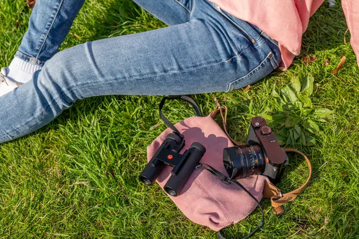 Woman sitting in the gras next to her Leica Noctivid Compact