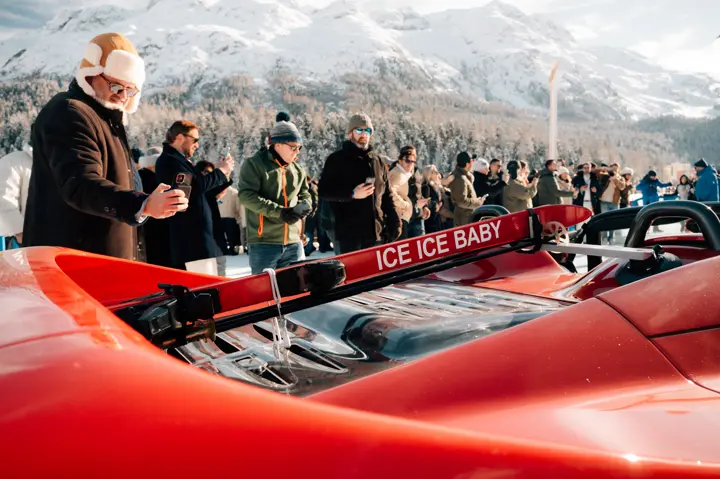 Red sports car in a snowy landscape with many men taking pictures of the car