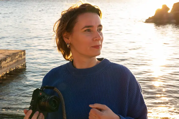 Julia stands with her Leica Q camera in front of the sea 