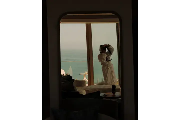 Julia Nimke capturing a self-portrait in a hotel suite overlooking the sea.