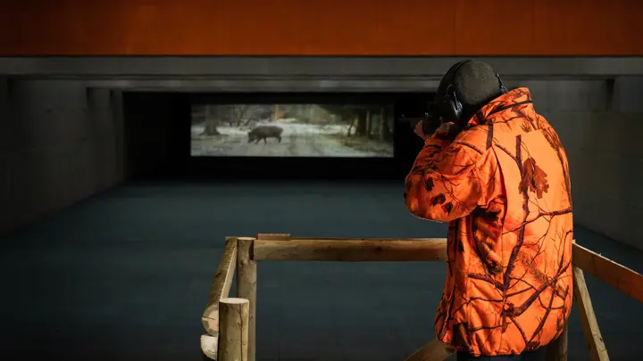 hunter-in-orange-camouflage-jacket-aiming-rifle-at-indoor-wild-boar-shooting-range