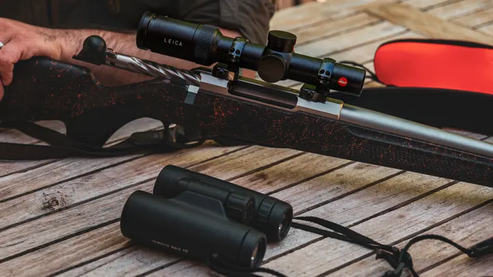 leica-rifle-scope-mounted-on-hunting-rifle-with-binoculars-on-wooden-table