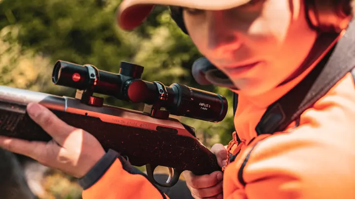 young-hunter-in-orange-jacket-aiming-rifle-with-leica-scope-outdoors