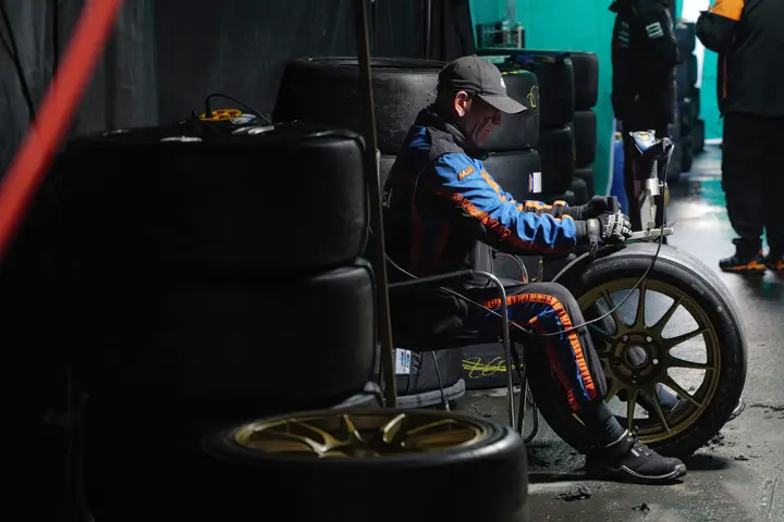 Motorsport crew member resting in the pit lane beside racing tires, highlighting the behind-the-scenes atmosphere of endurance racing.