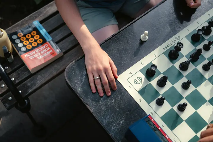 Close-up of an outdoor chess game with a chess clock and strategy book.