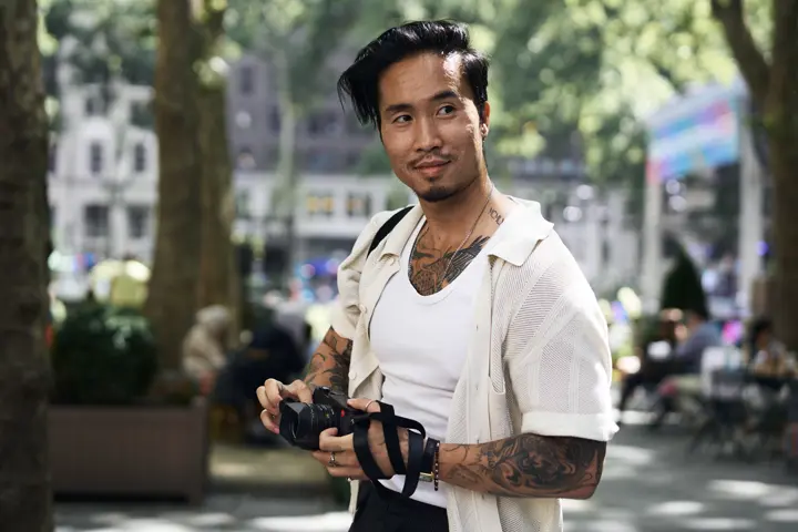 Street photographer Billy Dinh holding a Leica Q in a New York City park, capturing candid moments and authentic urban life through documentary photography.