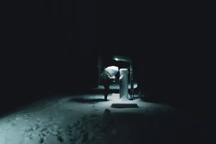 A man beneath the glow of a parking payment machine on a snowy night.