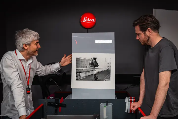 Two people examining a black-and-white print in a darkroom.