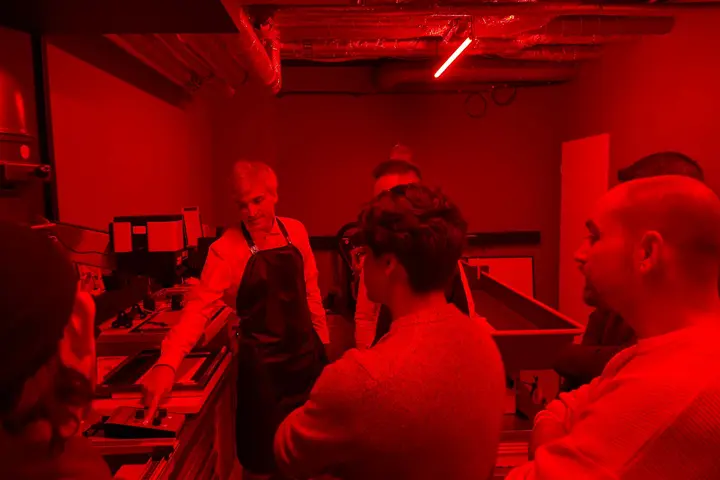Group learning traditional photo development techniques in a red-lit darkroom.
