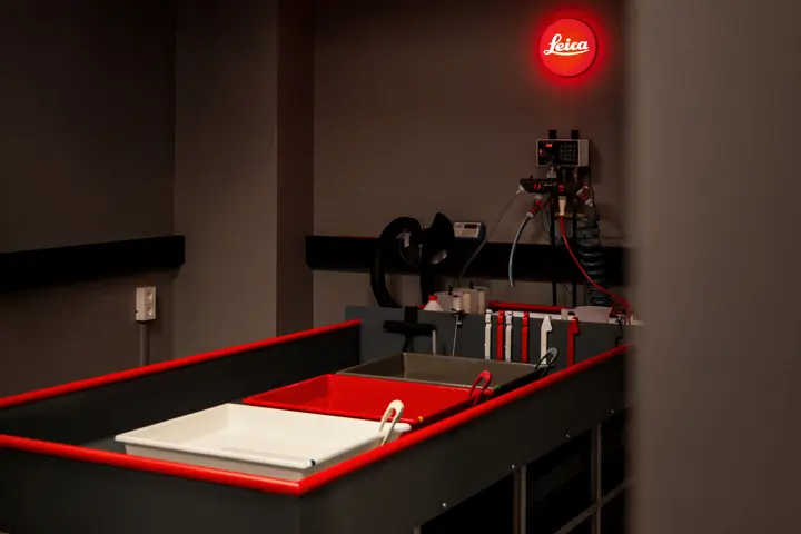 Darkroom equipment with developing trays beneath an illuminated Leica logo.