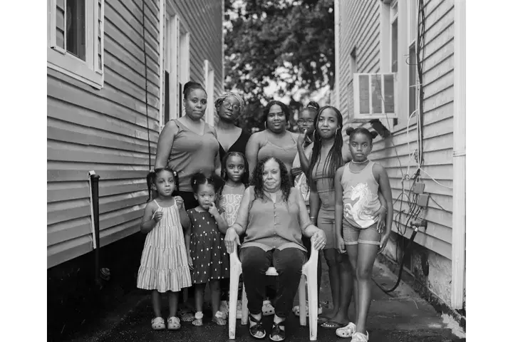 Black-and-white group portrait of women and girls of different generations gathered between two houses.