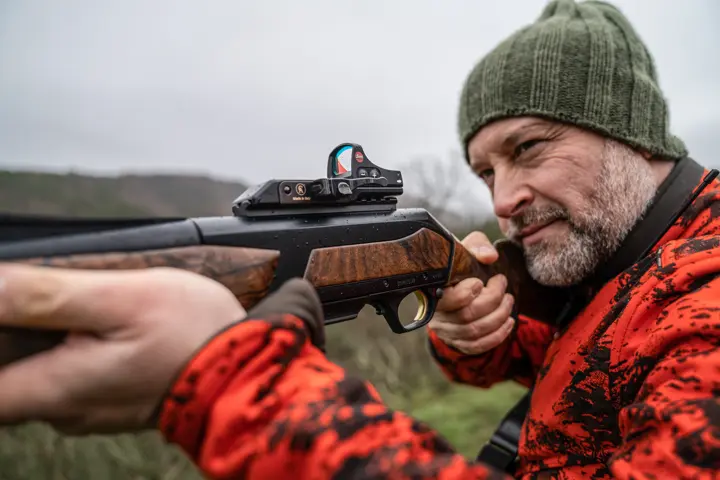 Close-up–of–a–hunter–aiming–a–rifle–with–a–Leica–Tempus–while–wearing–orange–camouflage–and–a–green–beanie–outdoors