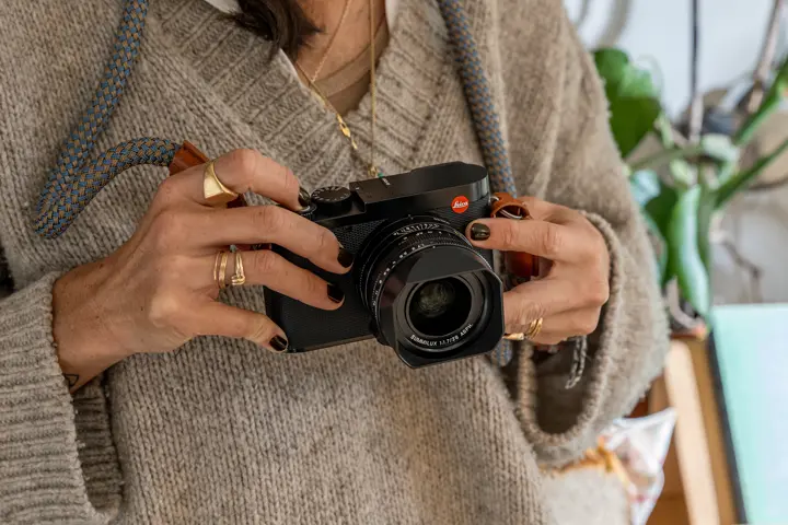 Woman holding a compact Leica Q camera indoors, with the camera and lens prominently in focus.