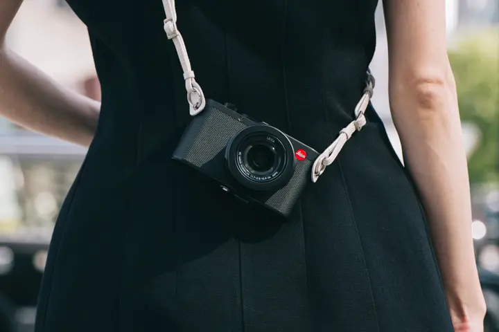 Compact Leica camera worn crossbody over a black dress, presented as a stylish everyday companion.