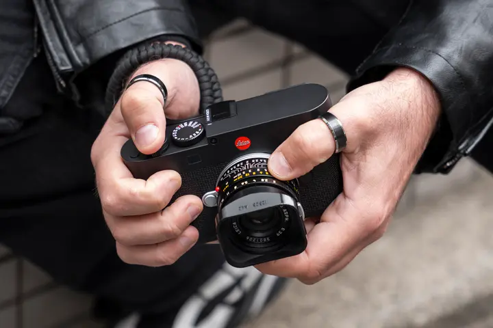 Leica M rangefinder in use — Close-up of a person in a black leather jacket adjusting the controls and lens of a black Leica M camera.