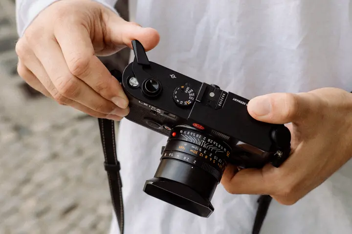 Classic Leica M film camera — Hands holding a vintage black Leica M rangefinder camera with a 35 mm lens and raised film advance lever.