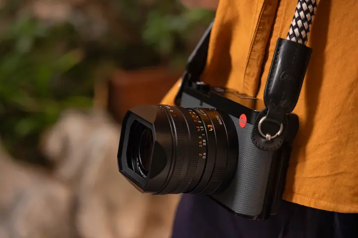 Leica Q3 43 worn on a strap — Close-up of a Leica Q3 43 camera with 43 mm lens hanging from a rope strap against a warm orange shirt.