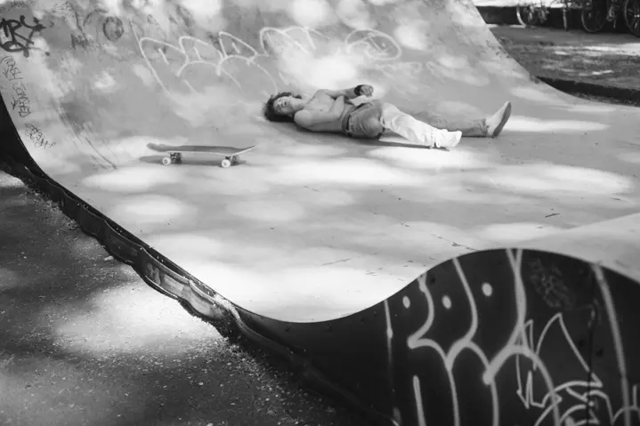 A skateboarder resting beside a skateboard in a graffiti-covered skate bowl, captured in soft dappled light.