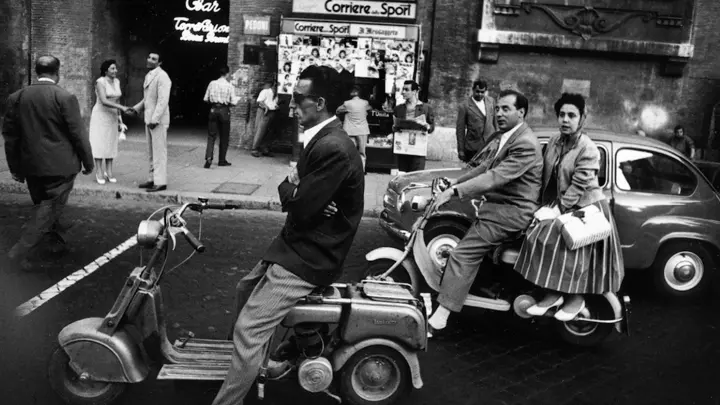 Black and white image of Rome in 1956 featuring man riding Vespa