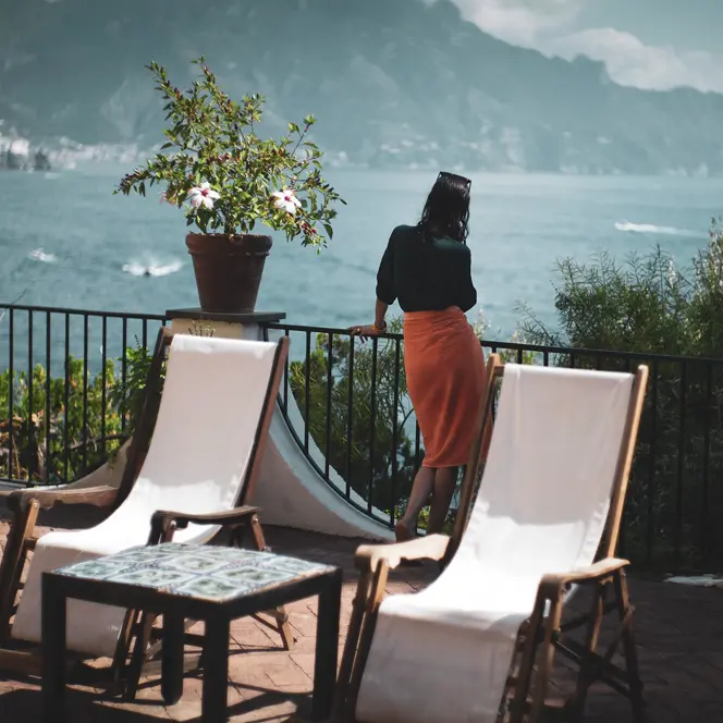 Woman on a large balcony with a view of a lake and mountains.