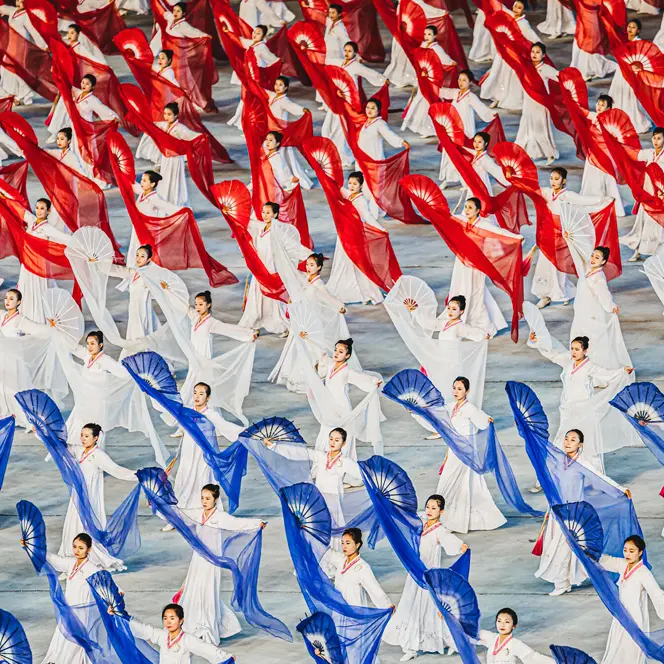 North Korean women dance with hand fans and transparent cloths in white, red and blue. 