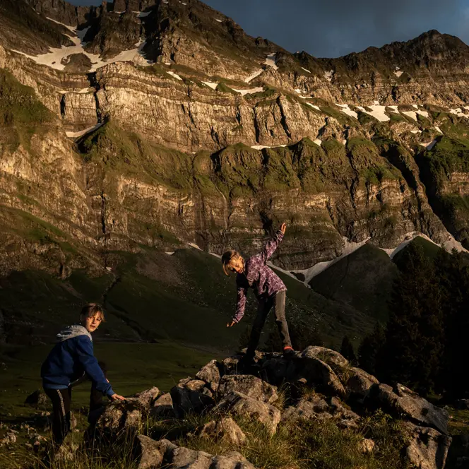 Two children climbing rocks in a mountain landscape at sunset.