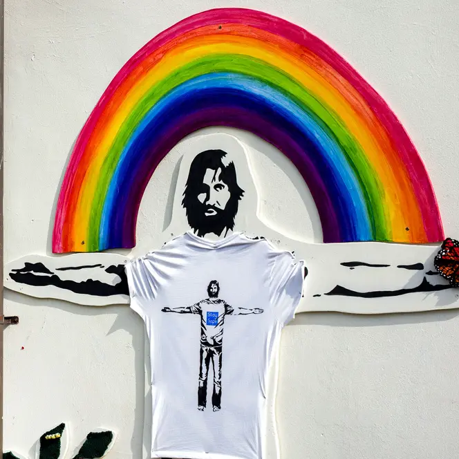 A mural on the wall of a man with outstretched arms in front of a rainbow.