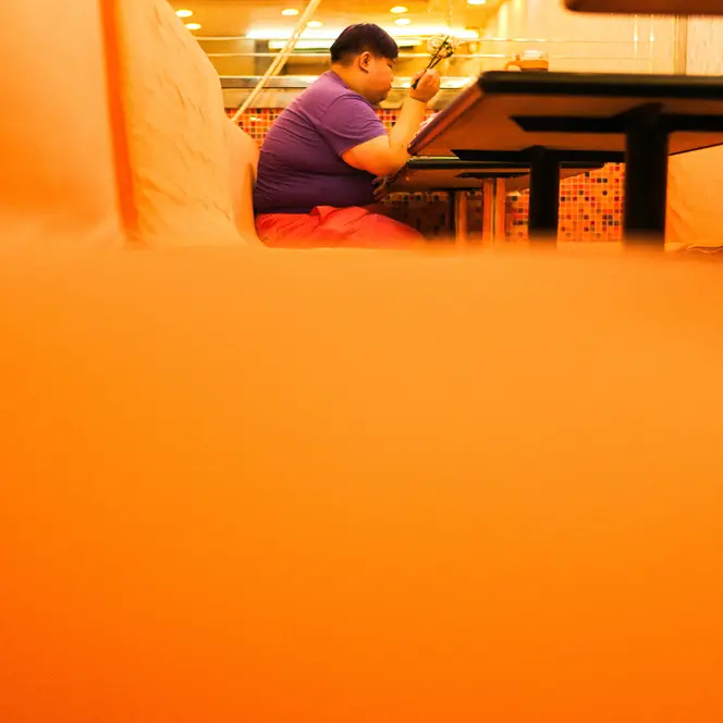 Close-up of an orange bench in a restaurant with a person sitting and eating in the background.