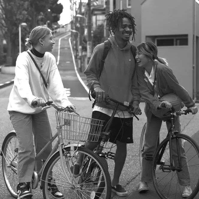 Three young people stand on bicycles in the street and laugh together.