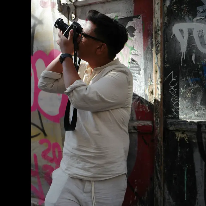 Patrick Domingo takes a photo standing in front of a graffiti wall.