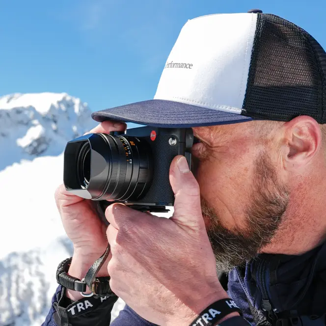 A man takes a photograph in a snowy mountain landscape.