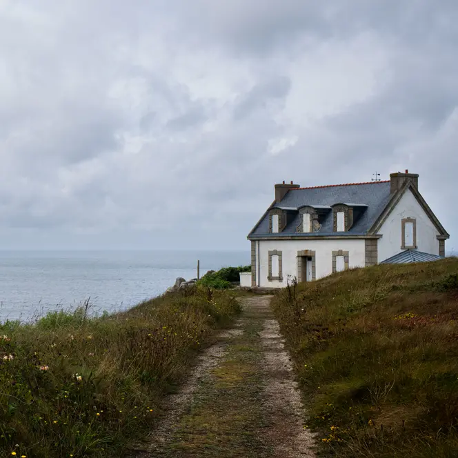 White house on a cliff, surrounded by flowers and a view of the cloudy sea.