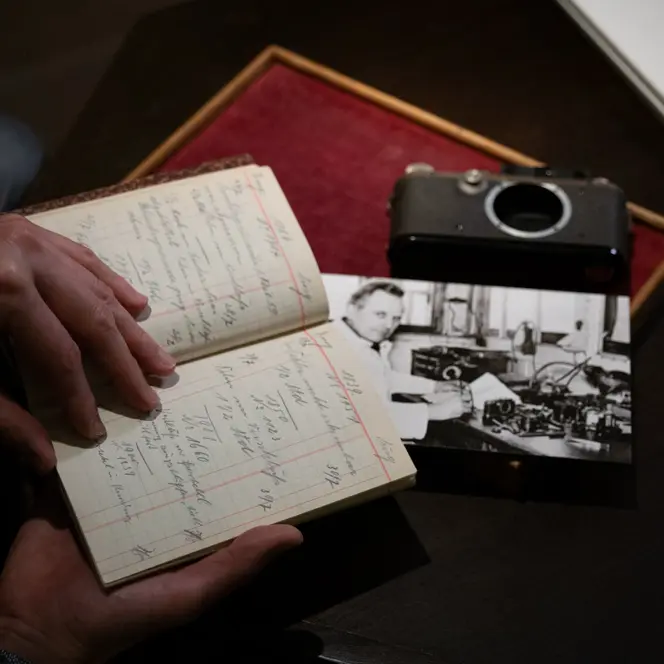 Person holding an old paper notebook, a photograph and a camera lie on the table.
