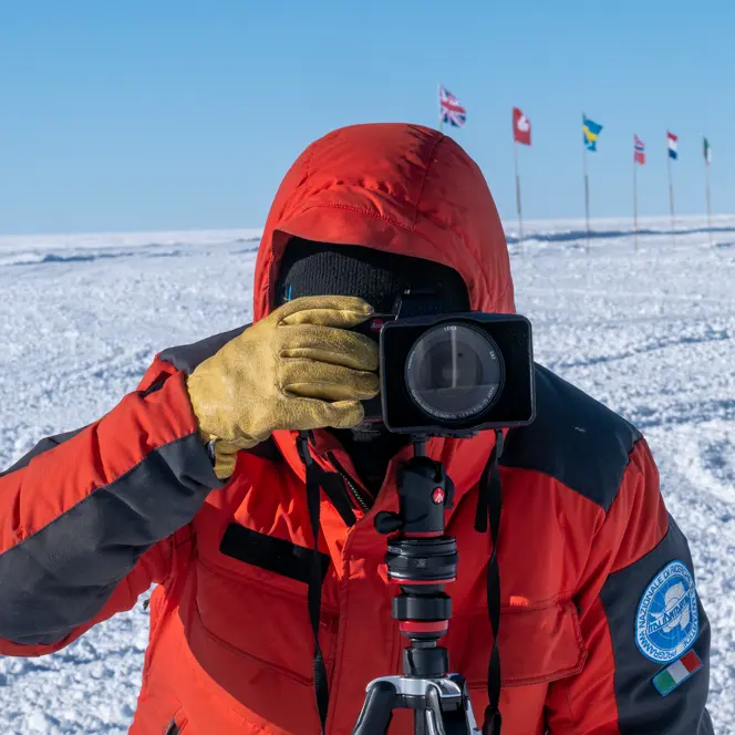 Person takes a photo in a snowy landscape with European flags in the background.