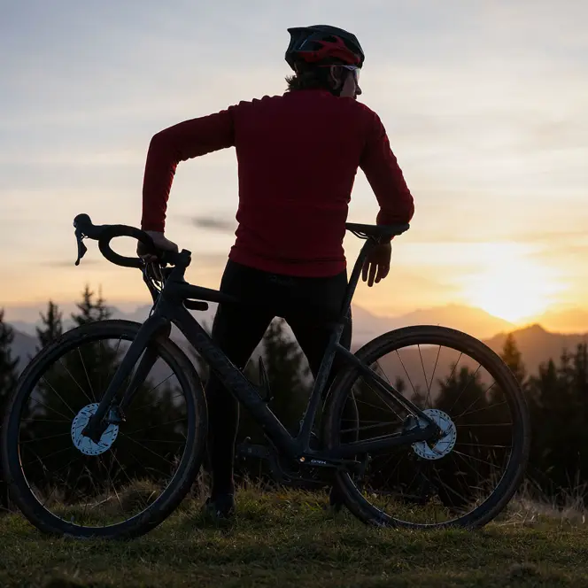 Man leaning on his mountain bike looking at the mountains at sunset.