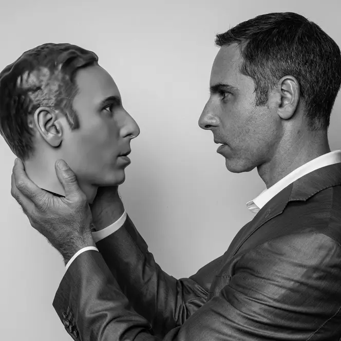 A man holds an artificial head in his hands and looks directly into its eyes.