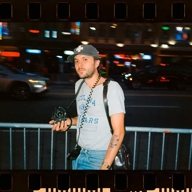 Joe Greer with a Leica M6 in his hand standing at a street at night.