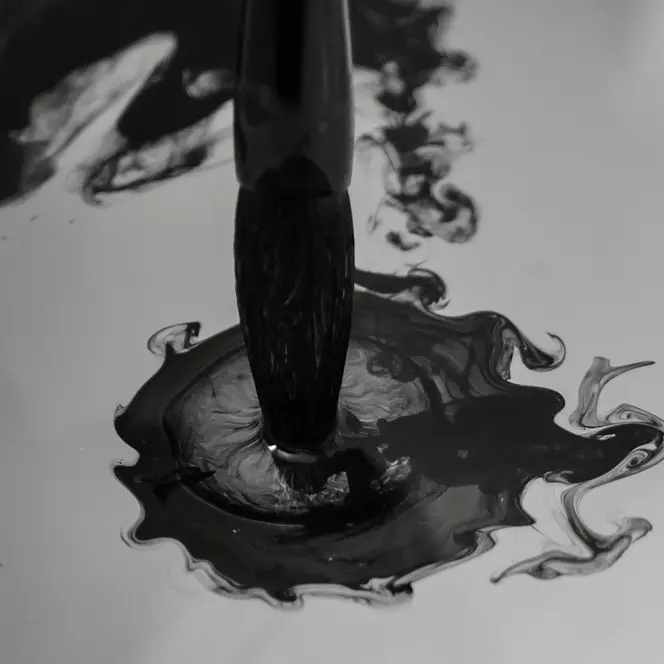 Brush dips into dark ink that spreads in the water.
