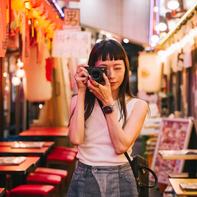 A woman takes pictures with a camera in a colorful, illuminated street.