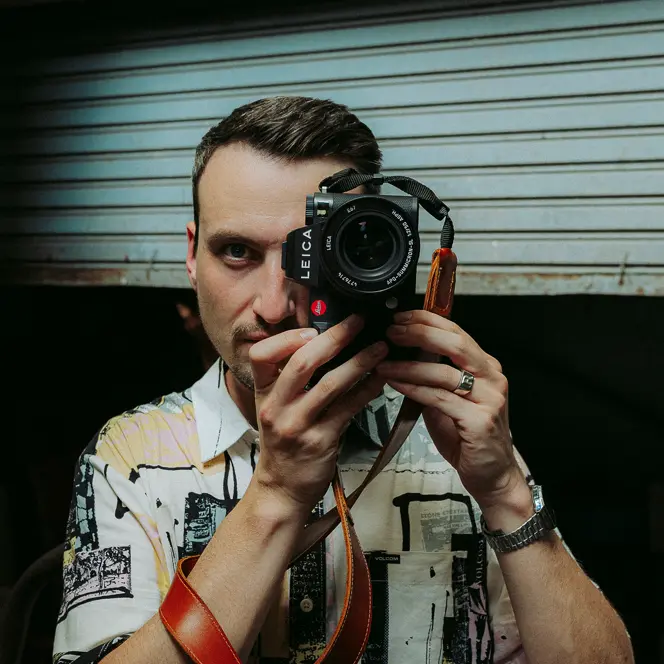 Philipp Reinhard looks through a camera and stands in front of a blue garage door.