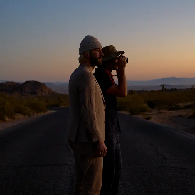 Garrett and Gantry Hill in a desert landscape at sunset, one looking through a camera.