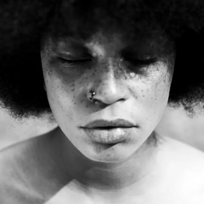 A close-up of a person with closed eyes and Afro hairstyle in black and white