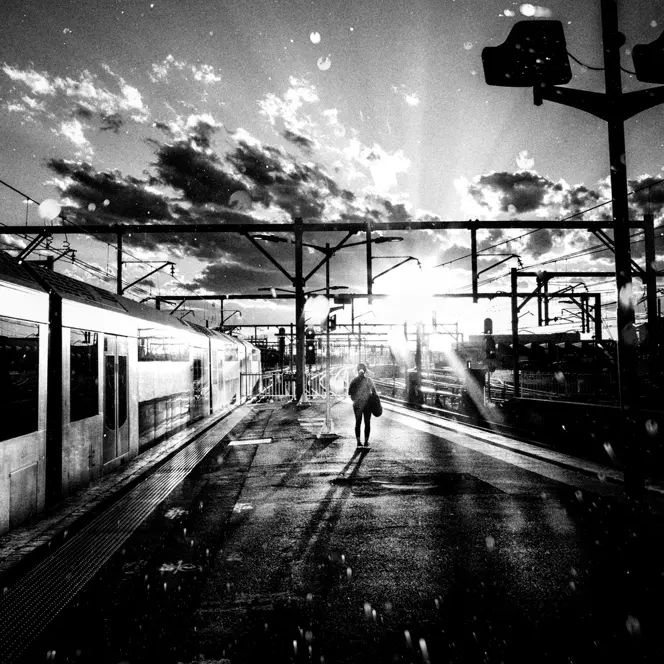 A person stands on a platform next to a train while the sun casts shadows.