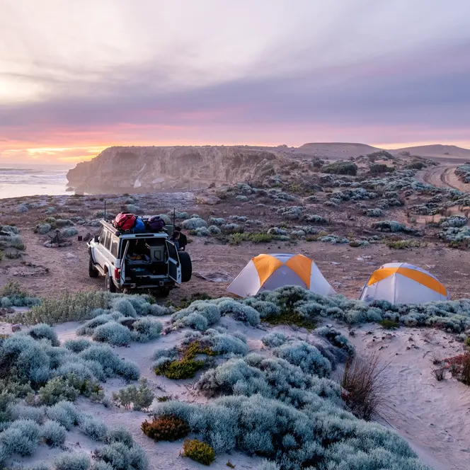 A jeep and two tents on a coast at sunset.