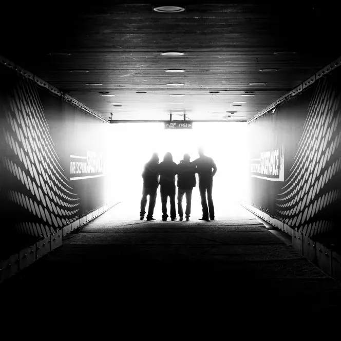 Four people are standing in a stadium tunnel with the sign "Stade France" in the light at the end of the corridor.