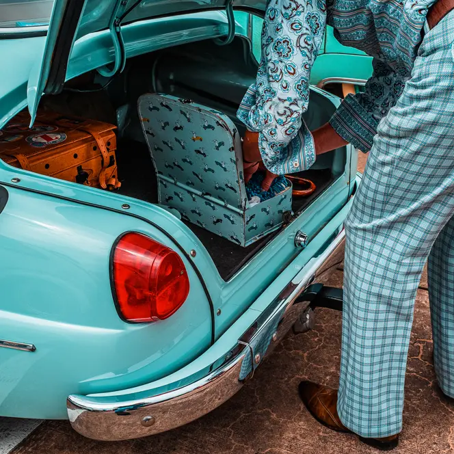 A person packs suitcases into the trunk of a turquoise vintage car.