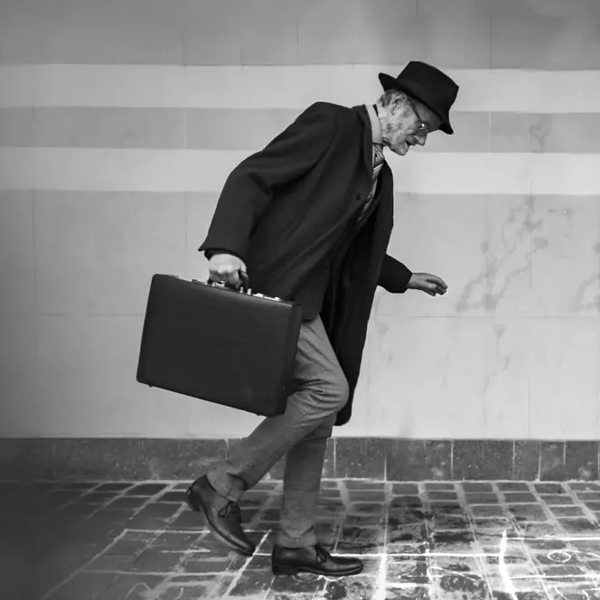 Elderly man in suit with hat and briefcase walking on icy cobblestones.