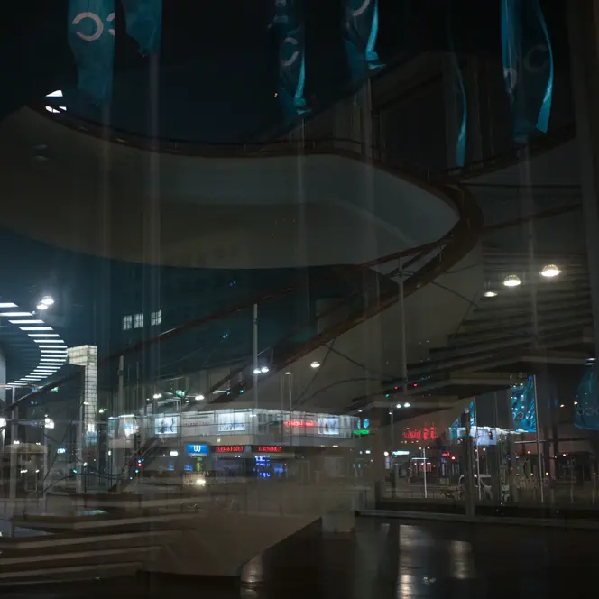 Reflection of a spiral staircase and a city at night in the glass front of a building.