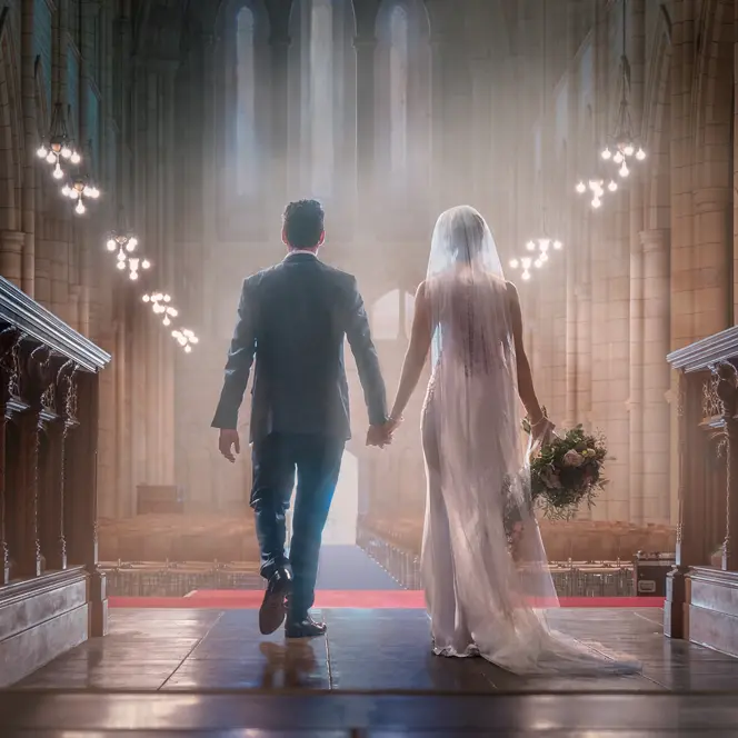 A bride and groom walk hand in hand down the aisle of an impressive church.