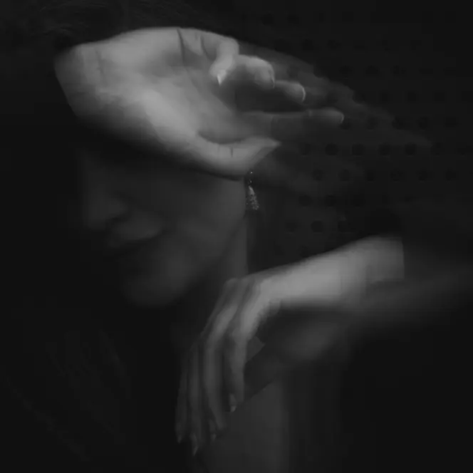 Blurred black and white image of a person covering her face with her arm.